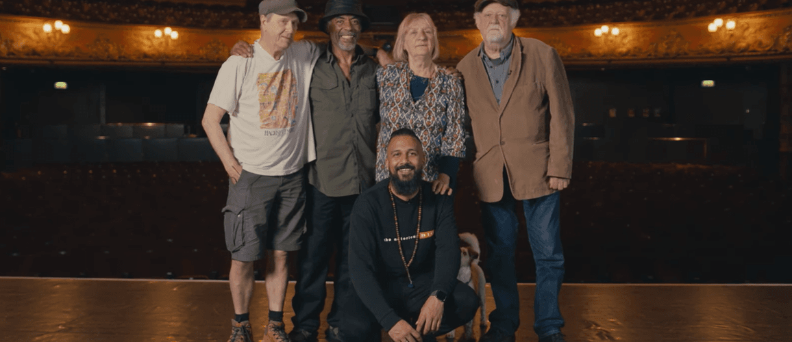 A photo of Brian Wren, Othman Read, Claire Muldoon, Roland Muldoon and Yamin Choudury posing together in the centre of Hackney Empire's stage with the auditorium behind.