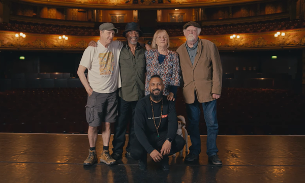 A photo of Brian Wren, Othman Read, Claire Muldoon, Roland Muldoon and Yamin Choudury posing together in the centre of Hackney Empire's stage with the auditorium behind.