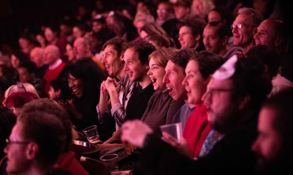 A photo taken along a row of people enjoying Mother Goose all with their faces smiling or amazed by what they're seeing.