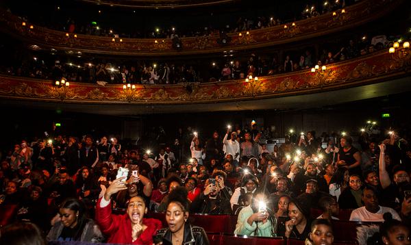 A photo of the Hackney Empire audience showing young people enjoying the act on stage with their camera lights on and held in the air.