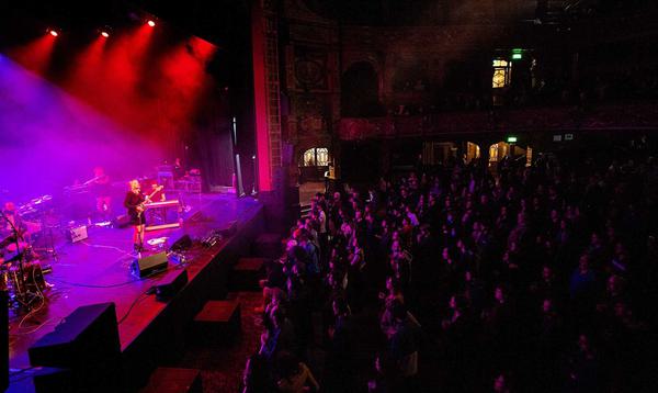 A photo of a standing audience for Cate Le Bon in 2022, taking from the side of the auditorium, showing Cate on stage and the audience watching.