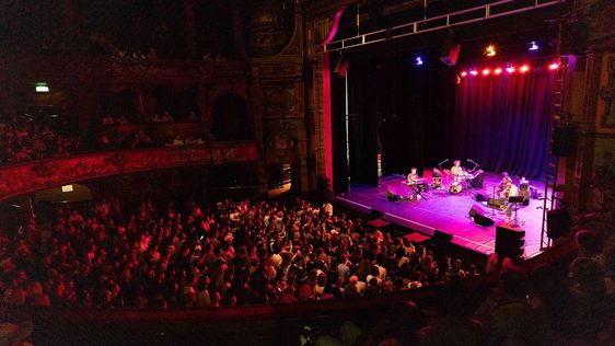 A photo taken from the side of the Dress Circle showing a full audience watching Mac DeMarco performing on stage.