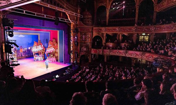 A photo taken from the Dress Circle showing Rishi Manuel on stage as Wishy Twankey and a whole crowd watching him.