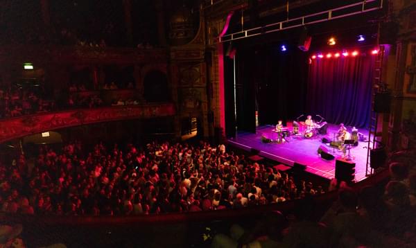 A photo taken from the side of the Dress Circle showing a full audience watching Mac DeMarco performing on stage.