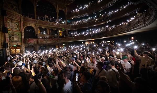 A photo of the auditorium of Hackney Empire showing a full crowd holding their phones in the air with their torches on.