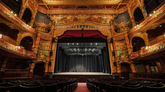 A photo of Hackney Empire from the back of the Stalls, showing the backs of the chairs, the auditorium and the whole stage.