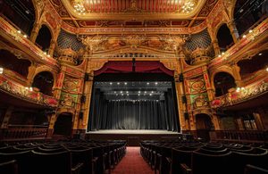 A photo of Hackney Empire from the back of the Stalls, showing the backs of the chairs, the auditorium and the whole stage.