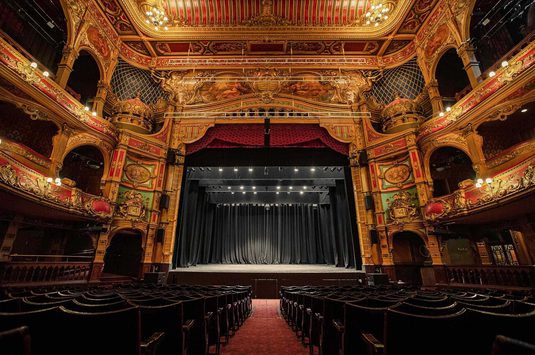 A photo of Hackney Empire from the back of the Stalls, showing the backs of the chairs, the auditorium and the whole stage.