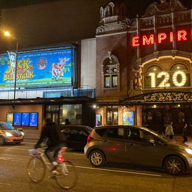 A photo taken of the outside of Hackney Empire from across the road showing the front of the building and the pantomime banner next to it.