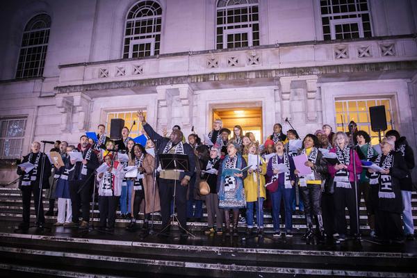 A photo of Hackney Empire community choir performing on the steps of Hackney Town Hall at Christmas time
