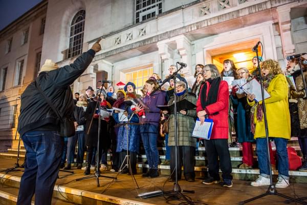A photo of Hackney Empire community choir performing on the steps of Hackney Town Hall at Christmas time