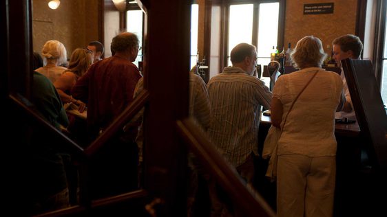 A photo taken through the doors looking into the Dress Circle bar, showing people waiting to collect their drinks.