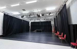 A photo of our rehearsal space Empire 2 showing the empty room with the black curtains pulled and red chairs along the side.