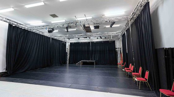 A photo of our rehearsal space Empire 2 showing the empty room with the black curtains pulled and red chairs along the side.