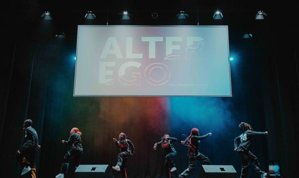 Dance group on stage preforming while the screen above them is showing the Alter Ego title
