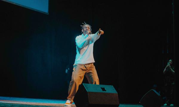 D1GZ on stage performing to the crowd with his arm pointed to the audiences