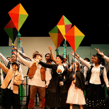 A group of Anna Fiorentini school kids are on stage holding colourful kites
