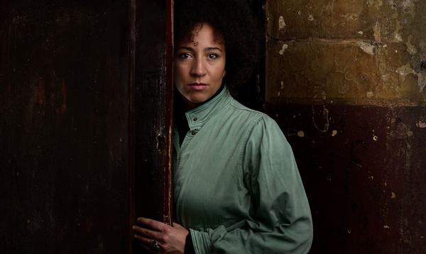 Christina Gill photographed at Shoreditch Town Hall stood halfway behind a door and wearing a blue top.