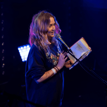 A photo of Hollie McNish reading from one of her books into a microphone.