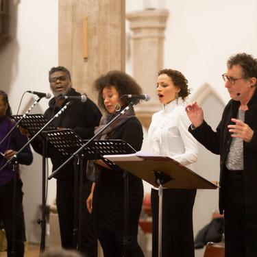 The Sun Does Shine soloists performing with the conductor. All are lined up and singing together.