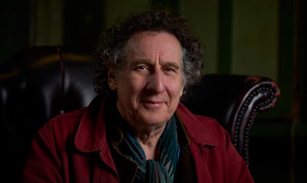 Harvey Brough photographed at Shoreditch Town Hall wearing a red jacket and smiling at the camera.