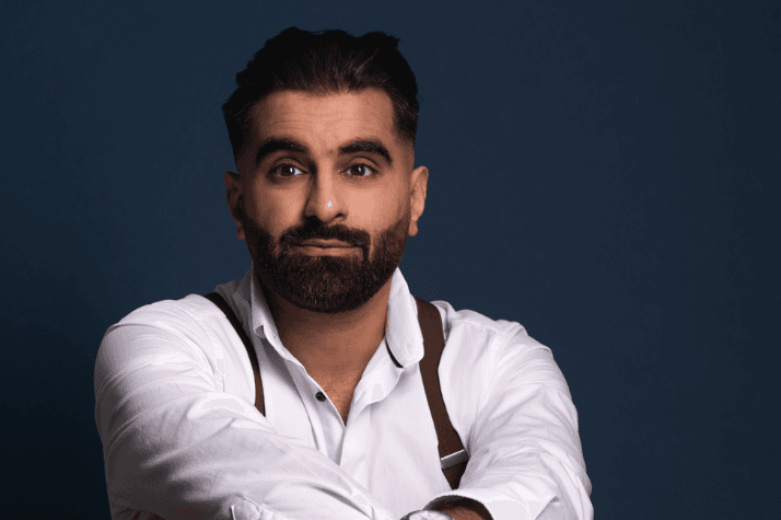 Tez is British Pakistani stand-up comedian, with short dark hair in a black tuxedo