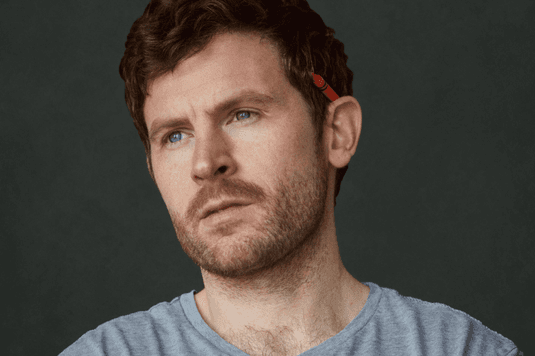 George Lewis is wearing a grey shirt and has a red pen sitting on the top of his ear.