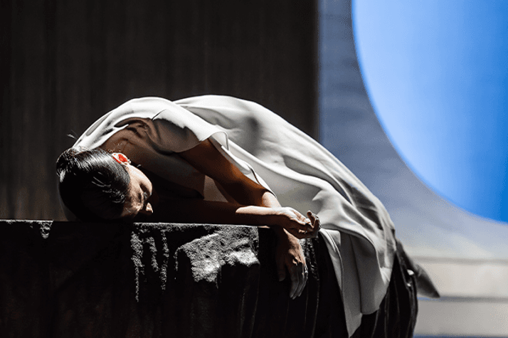 A woman wearing a white dress is laying face down on a stone bench