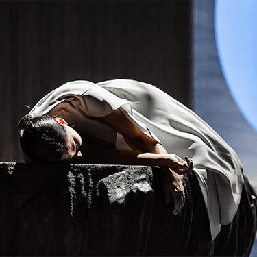 A woman wearing a white dress is laying face down on a stone bench