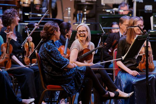 The violinists in City of London Sinfonia are smiling and laughing at each other.