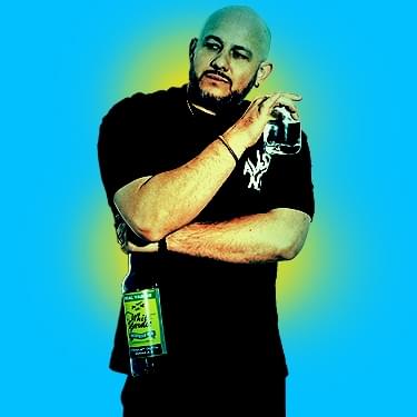 White Yardie is wearing a black top and is standing up straight with his arms crossed against his chest while holding a glass in one hand