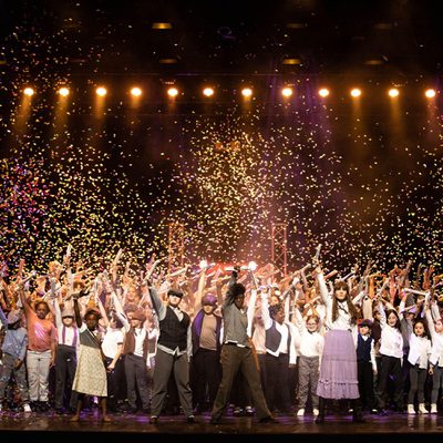 A group of people celebrating on stage as colorful confetti falls around them, creating a festive atmosphere.