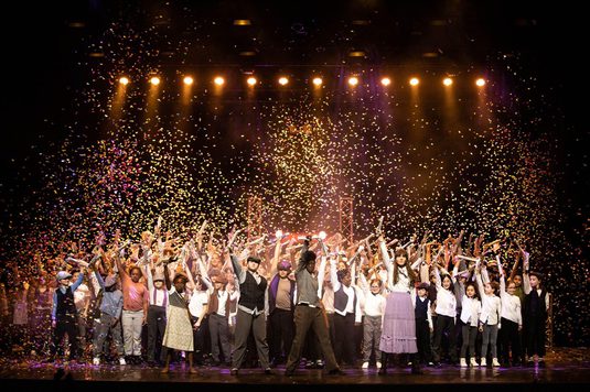 A group of people celebrating on stage as colorful confetti falls around them, creating a festive atmosphere.