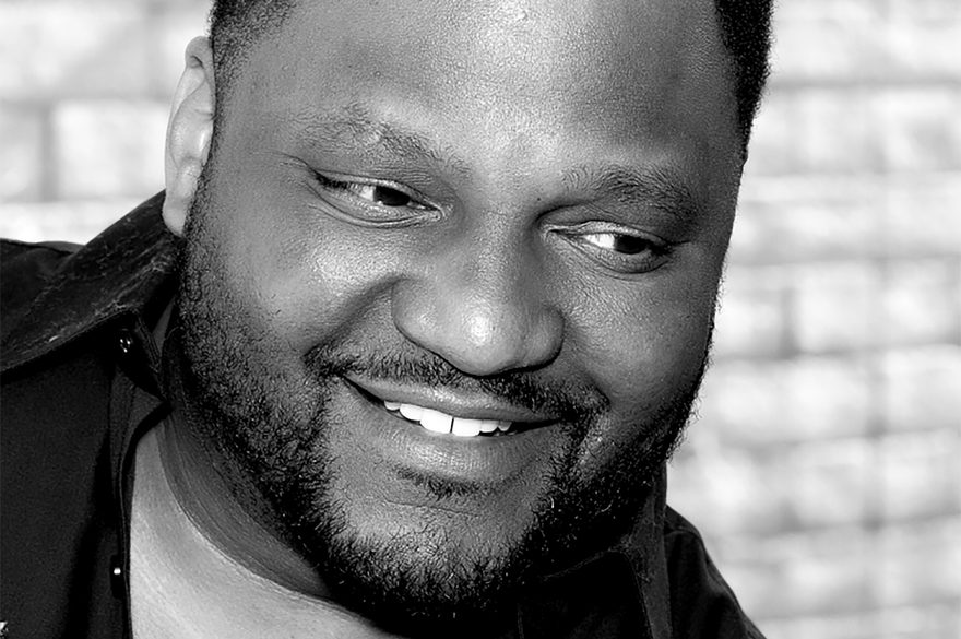 A close up photo of Aries Spears smiling in black and white.