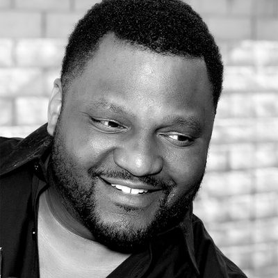 A close up photo of Aries Spears smiling in black and white.