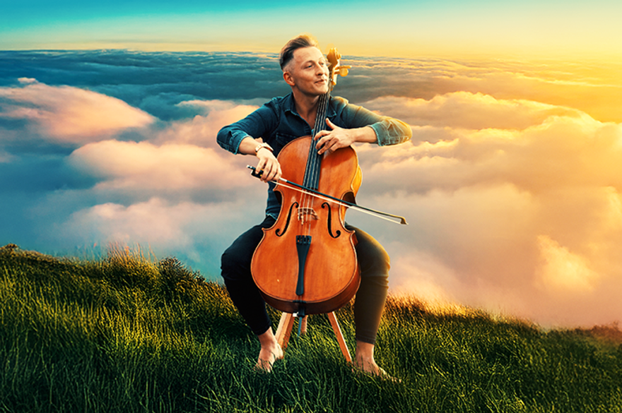 A musician plays a cello while seated on a grassy hill above the clouds, with a vibrant sunset illuminating the scene.