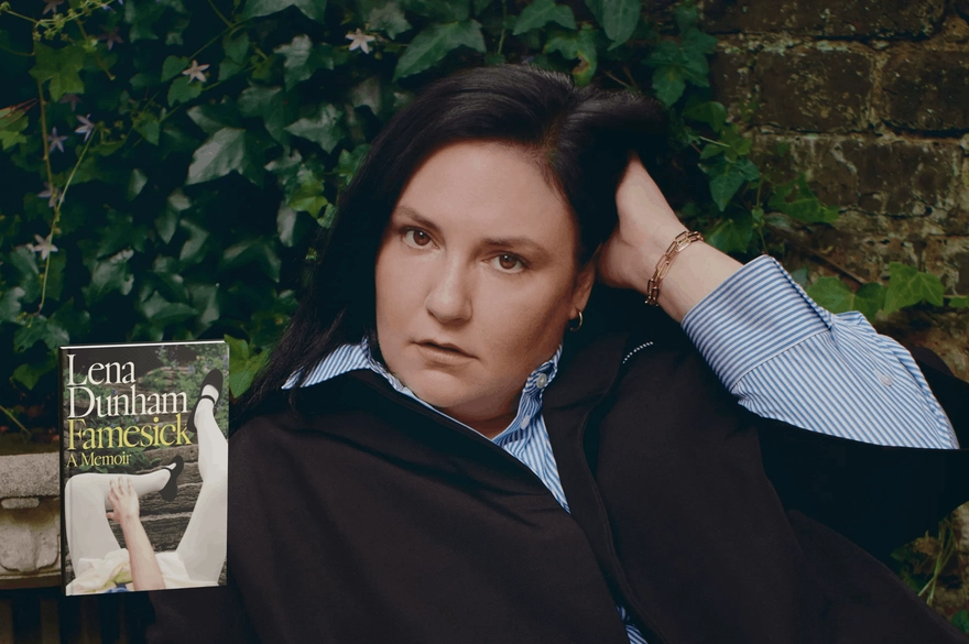 Lena Dunham, a white woman with brown eyes, is sweeping her long, dark brown hair back with her left hand. She is wearing a blue button-down shirt and a black jacket on top. There is a garden wall and ivy in the background. The cover of her memoir is superimposed on the bottom right-hand side. It shows a young woman dressed in a pale skirt, white tights and black mary jane shoes falling down the stairs of a garden path.