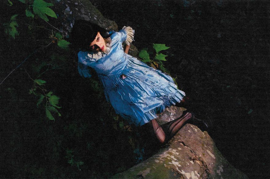 An aerial shot, looking down on María Zardoya lying on a raised tree branch, wearing a blue dress.