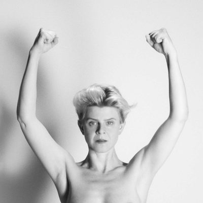 Robyn poses with her arms up, conveying a sense of empowerment and openness in a simple environment.