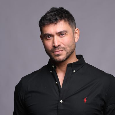 Rav wilding is wearing a black short with a red Ralph Lauren logo on the chest area and is looking straight into the camera whle standing agaisnt a light grey wall.