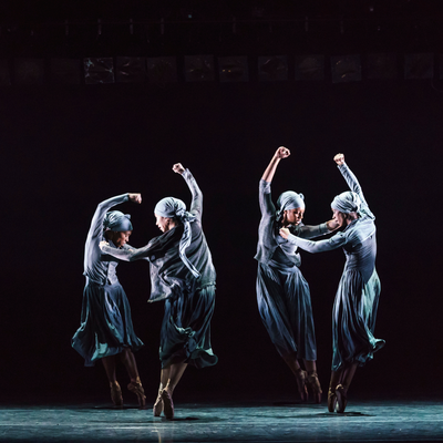 A group of four dancers wearing blue dresses elegantly performing together on stage in a vibrant setting.