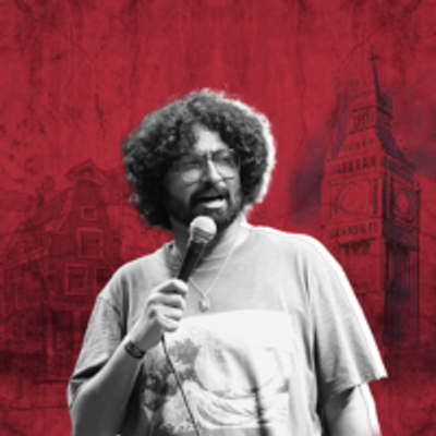 Ravi Gupta has big curly hair and is wearing glasses while holding a microphone, ready to speak or perform.