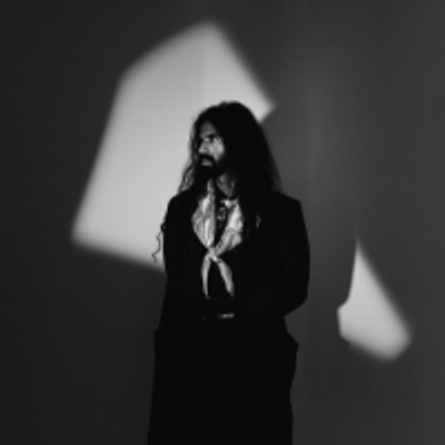 Vidura Bandara Rajapaksa is wearing all black and is standing in the dark. The light from the window is hitting his face