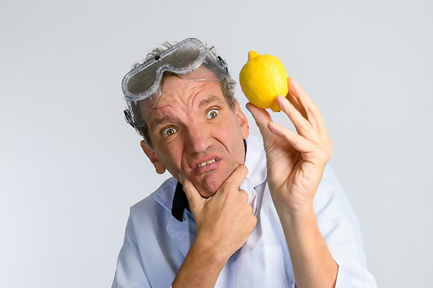Henning When is wearing a lab coat is holding a lemon, possibly for a scientific experiment or demonstration.
