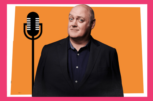 A promotional-style graphic featuring Dara Ó Briain in a dark blazer and navy shirt standing in front of an orange rectangle with a white border on a bright pink background. A large black microphone icon appears on the left side, suggesting a podcast, radio, or comedy performance theme.