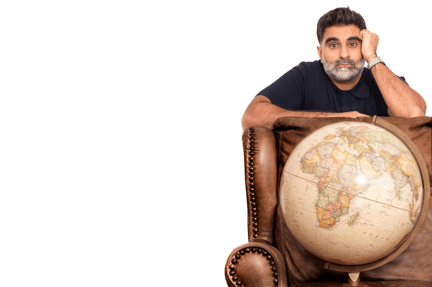 Tez Ilyas is sitting down with a globe on his chair, representing a connection to the world and global knowledge.