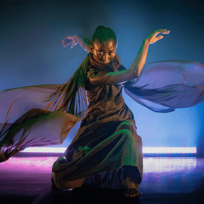 A woman in a flowing dress dances gracefully on stage, showcasing her talent and passion for performance.