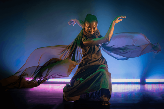 A woman in a flowing dress dances gracefully on stage, showcasing her talent and passion for performance.