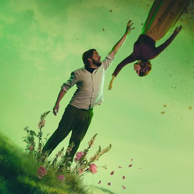 Two figures stand suspended against a green misty landscape. A man reaches upwards towards a woman who is floating upside down above him. Their outstretched hands nearly meet. Behind them, a hazy green sky or mist creates an ethereal atmosphere, with dark, textured rock formations framing the upper edge of the image