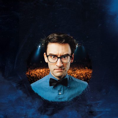 MC Hammersmith is wearing glasses, a blue shirt, and a black bow tie looks straight into the camera with a mean look on his face